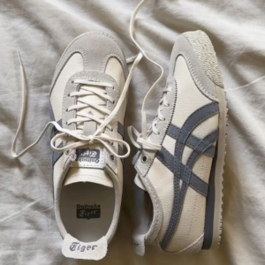 White and grey Onitsuka Tiger Mexico 66 sneakers placed on fabric background showing classic design and lace-up style